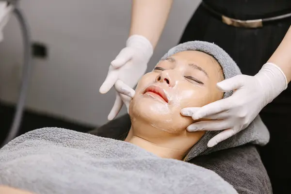 Woman facial massage face skin treatment with natural essence herbal extract moisturising cream in beauty spa clinic.