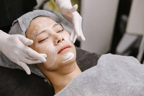 Woman facial massage face skin treatment with natural essence herbal extract moisturising cream in beauty spa clinic.