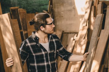 Katılımcı mobilya üreticisi yeni projeler için uygun ahşap parçası bulmak için odun yığınından malzeme seçin.