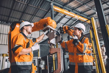 Otomasyon fabrikasında çalışan mühendis ekip servis robotu. Güvenlik kıyafeti giyen insanlar robotik kol yazılım programlama ya da otomatikleştirilmiş imalat endüstrisi teknolojisinde yer değiştirme işinde çalışıyorlar..