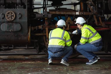 Mühendislik ekibi bakım onarımı eski bozuk mazot buharlı tren parkı demiryolu deposu ekibi güvenlik giysisiyle çalışıyor..