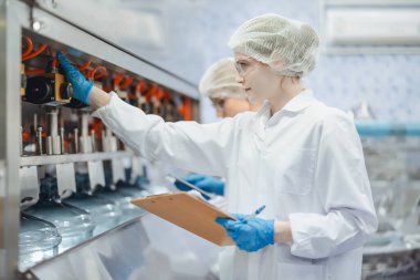 Su fabrikasında çalışan beyaz kadın işçiler içme suyu içme makinesi hattının şişelenmesinde temiz hijyen sürecinde.