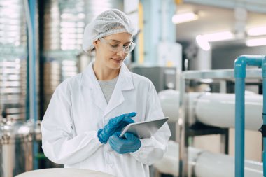 Mutlu kıdemli bilim kadrosu kadın çalışanı içme suyu fabrikasında suyun kalitesini kontrol etmek için iş kaydetmek için tablet kullanıyor..