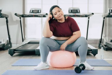 Ayrıca soru sormayı düşünen cüsseli kadınlar, spor kulübü fitness stüdyosunda oturan Asyalı şişman kadın.