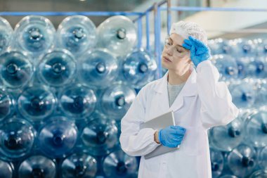 Yetişkin kadın frenleri gevşer yiyecek ve içecek fabrikasında çalışır su fabrikası işçisi yorgun jestler yapar..