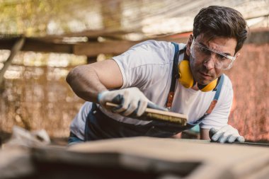 Marangoz adam ahşap atölyede ahşap mobilya yapmak için el işi ustalığı ile uğraşır..