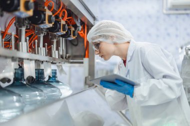 Kadın işçiler içme suyu fabrikasında çalışıyor. Kaliteli içme suyu doldurma makinesini kontrol ediyorlar.