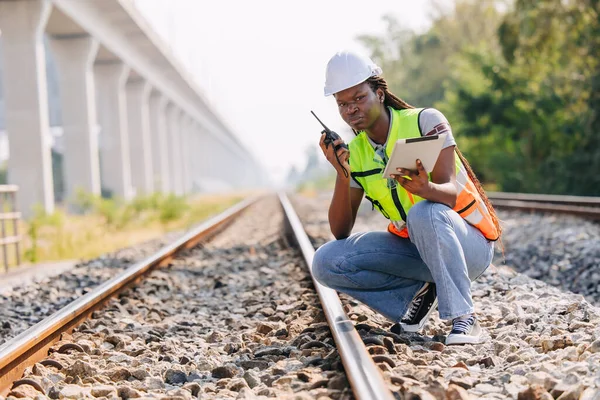 African black engineer women worker work checking service in train railway tracks construction site in transportation industry radio operate
