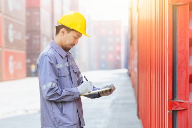 Asyalı erkek gümrük işçisi liman tersanesinde kargo konteynırı yüklerken akıllı çalışıyor. Japon nakliye sektörü personeli görev başında..