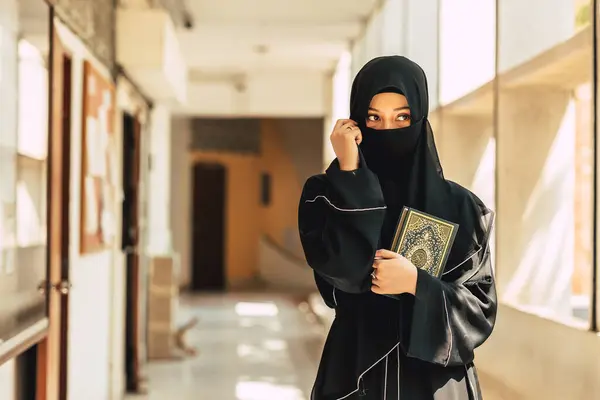 ムスリムのニカブの女性はクルアーンと信仰を学び 聖クルアーン書を読みました アラビアのサウジアラビアの黒の大使の女性 アラビアの書道はアルコーランの意味を翻訳します ロイヤリティフリーのストック写真