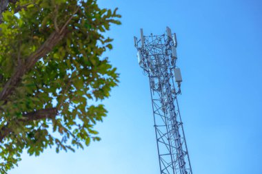 Açık havada 5G iletişim kulesi dijital kablosuz radyo sinyali mavi gökyüzünde yeşil ağaçlı uzun menzilli iletim hücresi konumu