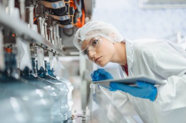 Kadın işçiler içme suyu fabrikasında çalışıyor. Kaliteli içme suyu doldurma makinesini kontrol ediyorlar.