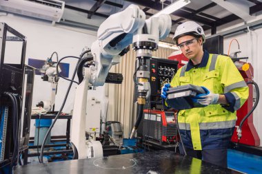 Mühendis genç üniversite öğrencisi endüstriyel robot kaynak kolunu robot mühendisleri laboratuvar sınıfında politeknik eğitimde kullanmayı öğreniyor..
