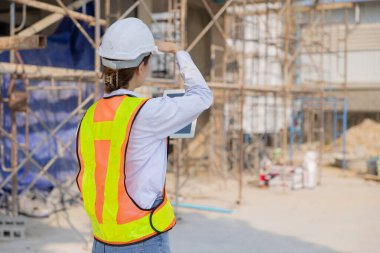 İnşaat alanındaki inşaat malzemelerini denetleyen sıkı şapka ve güvenlik yeleği olan genç bir kadın inşaat işçisi..