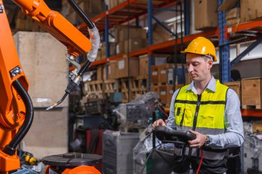 Güvenlik teçhizatlı bir mühendis üretim deposunda endüstriyel bir robotu çalıştırmak için kontrol paneli kullanıyor. Modern teknoloji, otomasyon ve mühendislik kavramı.