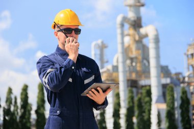 Petrol endüstrisi mühendisi dışarıda çalışıyor. Rafineri yağı ve gaz servisi ustabaşı tablet ve telsizle karmaşık gaz boru binasının bakımını üstleniyor..