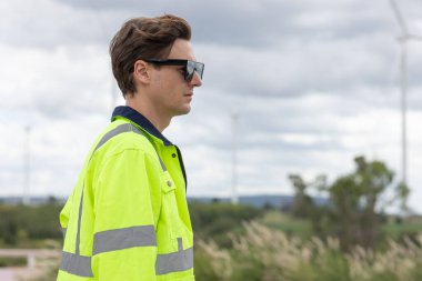 Akıllı, genç mühendis erkek işçi. Rüzgâr Türbinleri 'nin temiz güç jeneratörü arka planında yan görüş..