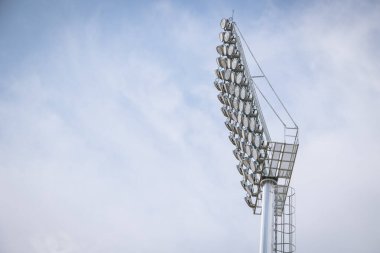 Stadyumun büyük ışıklarıyla, mavi gökyüzüne karşı bir spor sahasının üzerindeki projektörlerle..