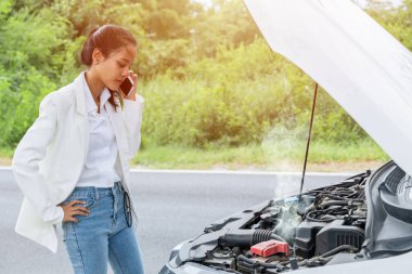 Genç bir kadın yolda bozuk bir arabayla yardım ve sigorta şirketini arıyor. Kızgın üzgün surat ifadesi..