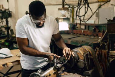 Afrikalı siyahi işçi ağır metal endüstrisi fabrikasında çalışıyor çelik parçası torna makinesiyle.