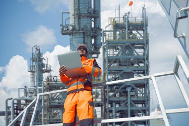 Profesyonel Petrol ve Petrol Rafineri işçisi Laptop bilgisayar monitörü enerji santrali kullanarak ham petrol damıtma kulesinde çalışıyor..