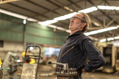 Kıdemli işçi yorgun kas ağrısı, bel ağrısı ağır sanayi fabrikasında sıkı çalışmaktan acı çekiyor..