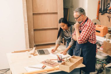 Profesyonel kıdemli marangoz kadın takımıyla çalışıyor fabrikadaki ahşap atölyede ahşap mobilya tasarımı yapıyor.