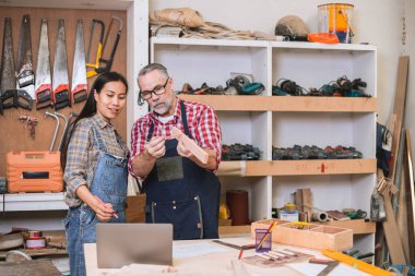 Profesyonel kıdemli marangoz kadın takımıyla çalışıyor fabrikadaki ahşap atölyede ahşap mobilya tasarımı yapıyor.