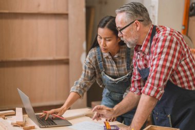 Profesyonel kıdemli marangoz kadın takımıyla çalışıyor fabrikadaki ahşap atölyede ahşap mobilya tasarımı yapıyor.