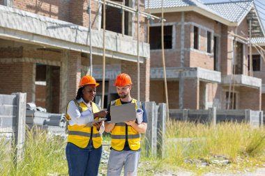 İnşaat işçisi inşaat sahasında çalışan Afrikalı siyahi kadın işçilerle konuşuyor. Dizüstü bilgisayarlı, müfettiş ekip çalışması için..