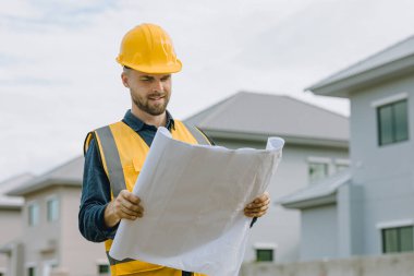 İnşaat işçisi mutlu bir şekilde gülümsüyor, inşaat alanında çelik yelek ve miğfer takan beyaz mühendis erkek..