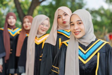 Bir grup Asyalı Müslüman kadın açık havada üniversiteyi tebrik ediyor. Bekar üniversite mezuniyet üniformalı Arap tesettürlü kız arkadaş.