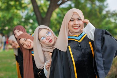 Bir grup Asyalı Müslüman kadın açık havada üniversiteyi tebrik ediyor. Bekar üniversite mezuniyet üniformalı Arap tesettürlü kız arkadaş.
