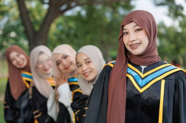 Bir grup Asyalı Müslüman kadın açık havada üniversiteyi tebrik ediyor. Bekar üniversite mezuniyet üniformalı Arap tesettürlü kız arkadaş.