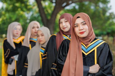 Bir grup Asyalı Müslüman kadın açık havada üniversiteyi tebrik ediyor. Bekar üniversite mezuniyet üniformalı Arap tesettürlü kız arkadaş.