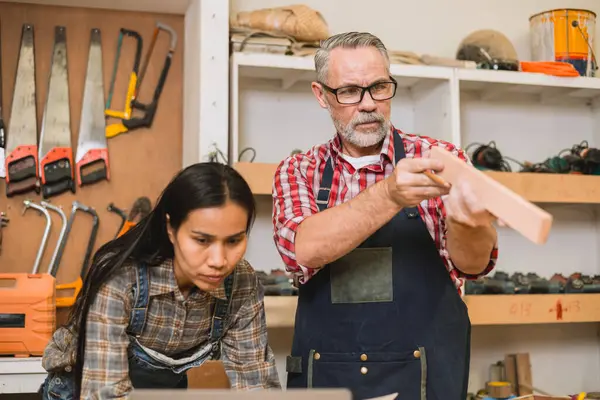 Profesyonel kıdemli marangoz kadın takımıyla çalışıyor fabrikadaki ahşap atölyede ahşap mobilya tasarımı yapıyor.