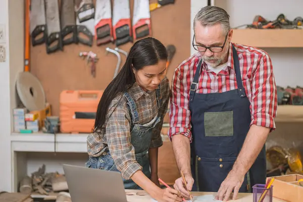 Profesyonel kıdemli marangoz kadın takımıyla çalışıyor fabrikadaki ahşap atölyede ahşap mobilya tasarımı yapıyor.