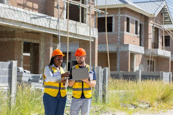 İnşaat işçisi inşaat sahasında çalışan Afrikalı siyahi kadın işçilerle konuşuyor. Dizüstü bilgisayarlı, müfettiş ekip çalışması için..
