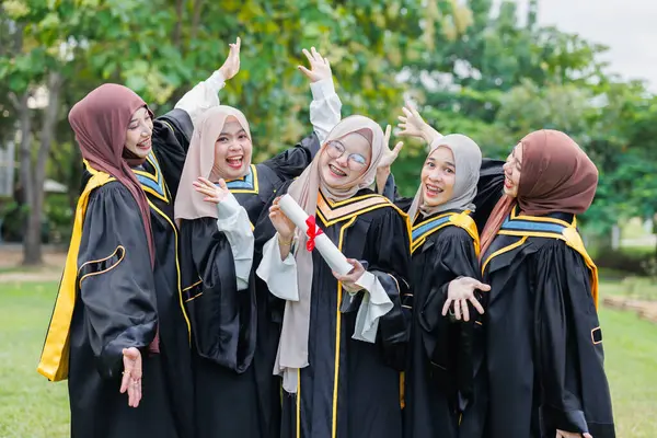 Bir grup Asyalı Müslüman kadın açık havada üniversiteyi tebrik ediyor. Bekar üniversite mezuniyet üniformalı Arap tesettürlü kız arkadaş.