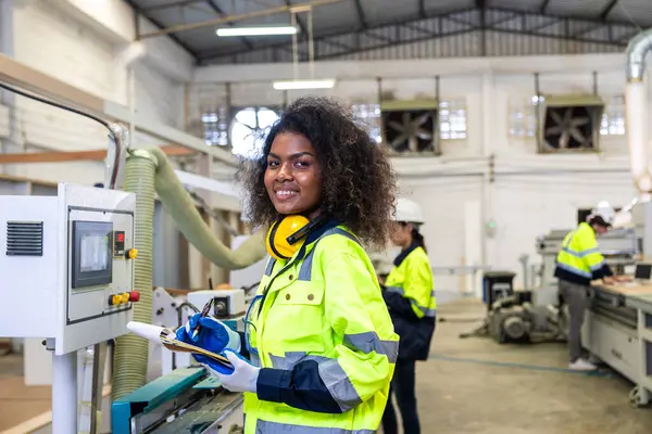 Portre Afrikalı siyahi kadın işçi ahşap kesiciyle çalışıyor mobilya fabrikası endüstrisi güvenlik kıyafeti ile mutlu gülümsüyor
