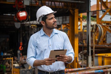 İspanyol asıllı Hintli inşaat mühendisi inşaat alanında güvenlik kaskı ve tablet bilgisayarla çalışan erkek işçi portresi.