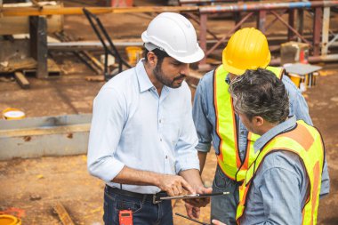 İnşaat mühendisi ekibi birlikte çalışıyor. Tablet bilgisayarla inşaat alanı planlama projesinde takım çalışmasına birlikte katılıyorlar.