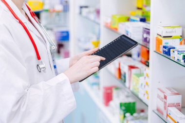 Eczacı, eczacı, tablet bilgisayar kullanan eczacı. Online akıllı cihaz veritabanı ile stoktaki ilaç raf yaşam detaylarını kontrol ediyor.