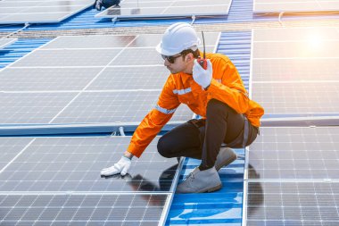 Sanayi binasının çatısına güneş panelleri kuran işçiler, yeşil eko enerji arzı için büyük ölçekli güneş enerjisi sistemi