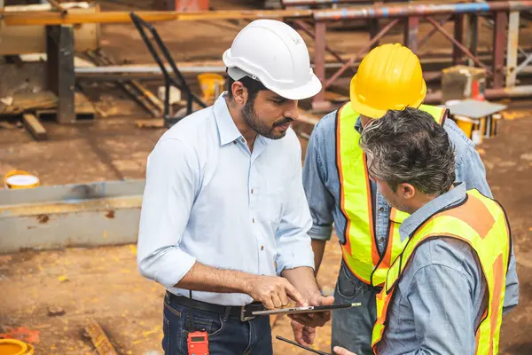 İnşaat mühendisi ekibi birlikte çalışıyor. Tablet bilgisayarla inşaat alanı planlama projesinde takım çalışmasına birlikte katılıyorlar.