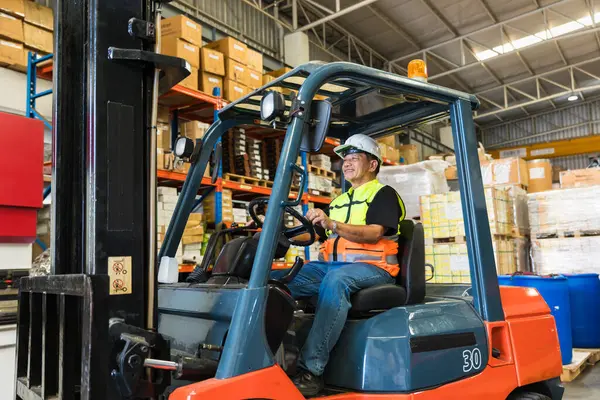 Depo işçisi forklift sürücüsü mutlu bir şekilde gülümsüyor çalışanların keyfini çıkarıyor. Asyalı erkek fabrika kargo işçisi