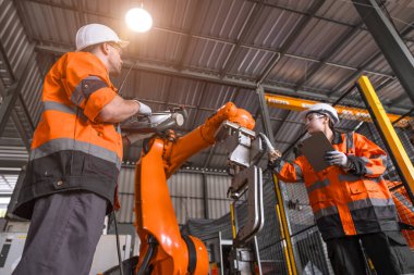 Teknisyen mühendis ekibi modern fabrikaya otomatik robot kol denetimi kurulumunu tamir etti. İşçiler tamir robotu parçasını kontrol ediyorlar.