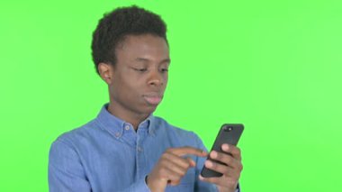Casual African Man Celebrating on Smartphone on Green Background