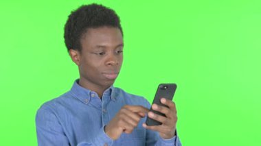 Casual African Man Browsing Smartphone on Green Background