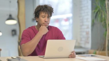 Young African Man Thinking while Working on Laptop